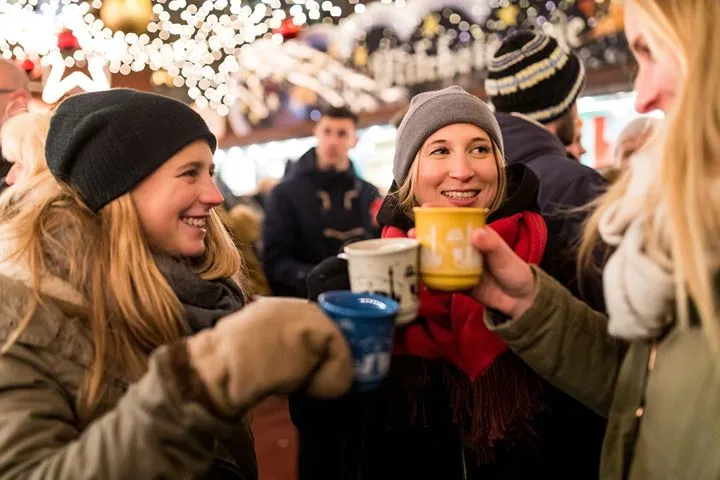 Friends toasting with warm drinks at a Christmas market in winter
